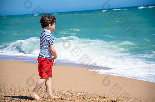 一个小孩在沙滩上玩耍，沙滩上的波浪滚滚而来。