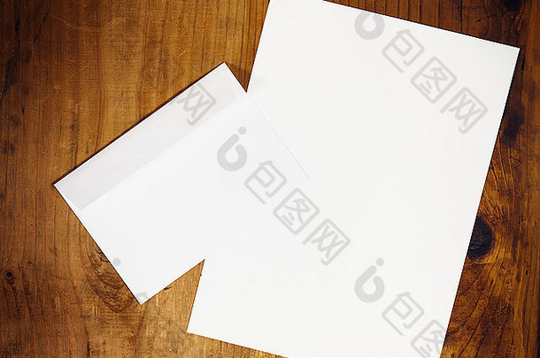 木质办公桌上的空白白色信封和信纸，复古色调，俯视图