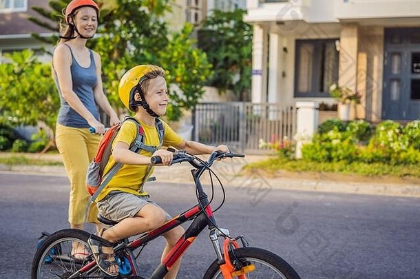 活跃的学校孩子男孩妈妈安全头盔骑自行车背包阳光明媚的一天快乐孩子骑自行车学校安全孩子们