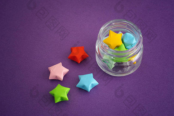 五颜六色的折纸幸运星从罐子里溢出。紫色背景。