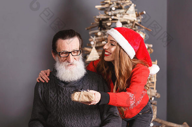 穿着红色毛衣、戴着<strong>圣诞</strong>帽的漂亮长发女儿给了她大胡子、穿着灰色毛衣的老爸爸一份<strong>圣诞</strong>礼物，他对这个新年、<strong>圣诞</strong>节、假期、纪念品、礼物、<strong>购</strong>物、折扣、商店、雪人<strong>圣诞</strong>老人、化妆、发型、<strong>狂欢</strong>节感到惊讶和高兴。