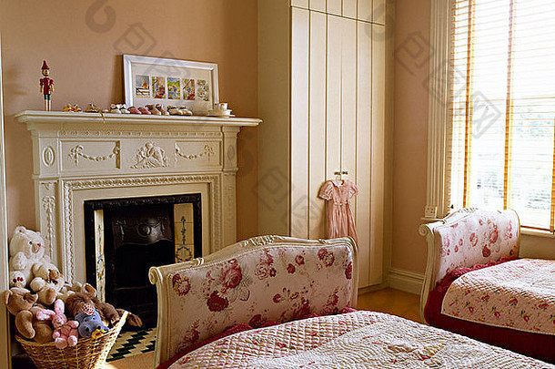 儿童卧室的双人床上有<strong>玫瑰</strong>图案的脚板和配套的被子，壁炉旁有一篮玩具