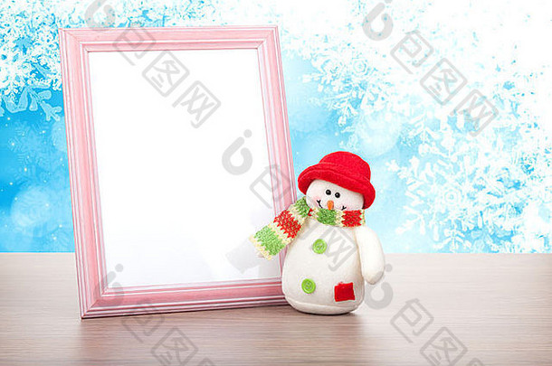 蓝色圣诞背景下木制桌子上的空白相框和圣诞雪人