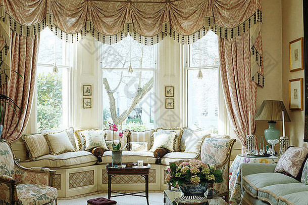 排屋客厅中，窗座上方的开间窗上挂着花边 尾丝<strong>窗帘</strong>，配有奶油软垫和舒适的沙发