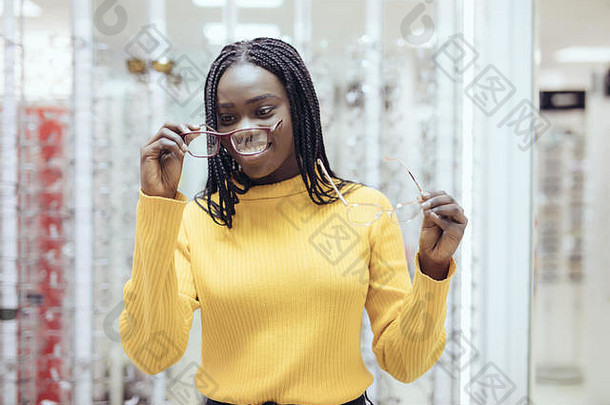在眼镜店，年轻漂亮的非洲女人在两个处方眼镜架之间选择。