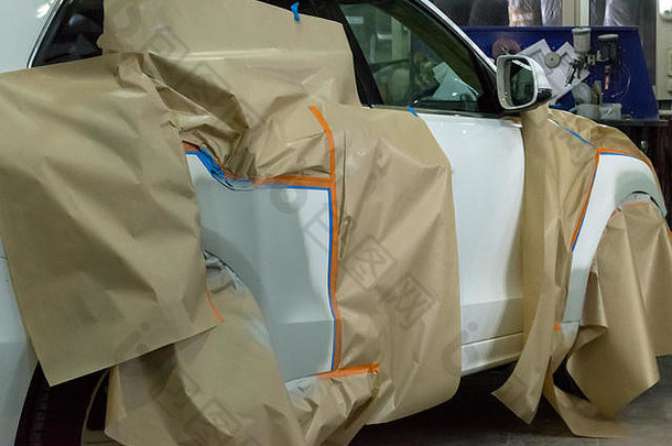 在车间为白色汽车喷漆以进行车身维修。SUV车上覆盖着纸，以免撞到油漆。