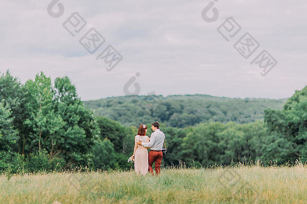 迷人的新娘和新郎独自站在草地上。拿着照相机的人。夏夜。