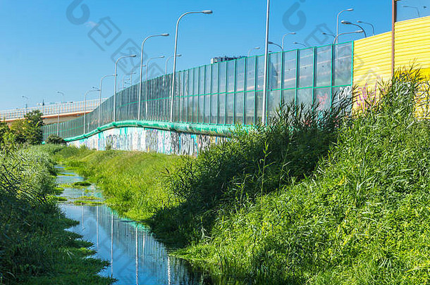 公路和小溪边的吸音屏。填充玻璃和黄色吸音板的金属框架。波兰的现代技术。