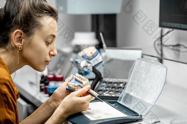 一名女技术员在实验室用刷子给假牙着色。种植体生产的概念