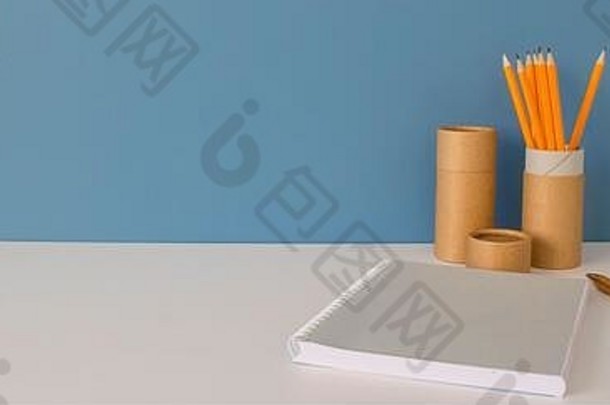 纸管，黄铅笔，笔记本和木笔，放在蓝色背景的白色桌子上。展示如何在家中重复使用纸管的回收概念