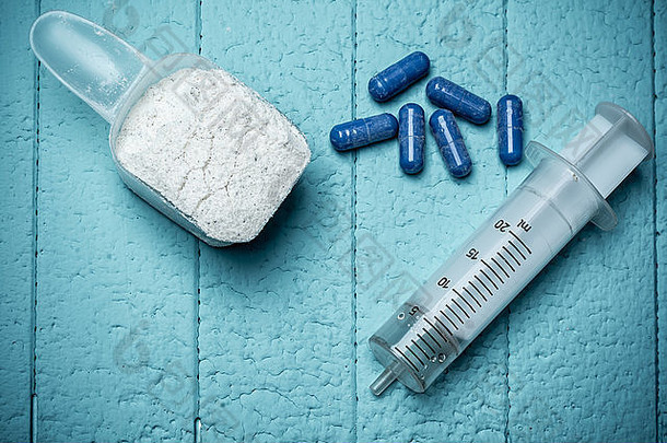 装牛奶乳清蛋白、空注射液和药丸的容器。特写。蓝色背景