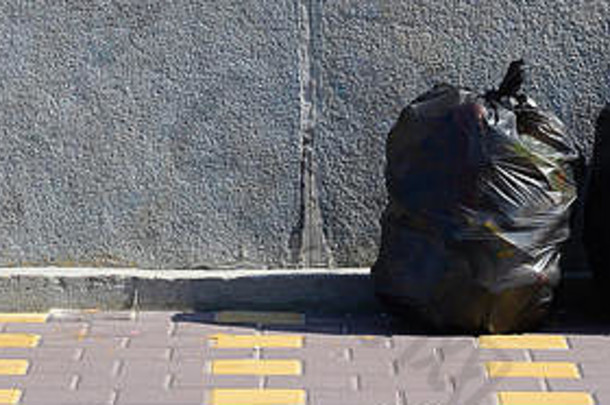 两个黑色垃圾袋<strong>放</strong>在城市水泥栅栏铺着<strong>瓷砖</strong>的街道地板<strong>上</strong>。污染垃圾