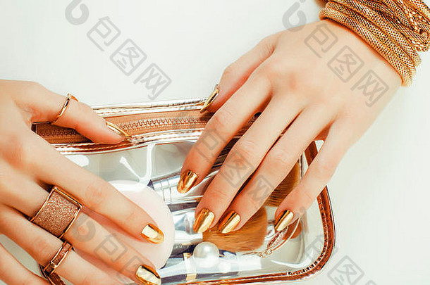 女人的手上有金色的指甲和许多拿着刷子的戒指，