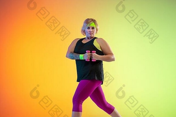 年轻的白人加大体型女模特在霓虹灯下的渐变橙色背景上训练。做举重锻炼。体育观念、健康生活方式、身体积极、平等。