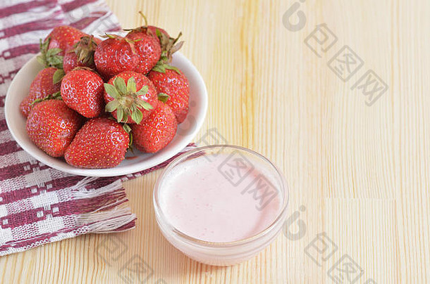 大草莓放在一个<strong>碟</strong>子上，站在一张铺着桌布的木桌上，旁边是一个奶<strong>油碟</strong>子