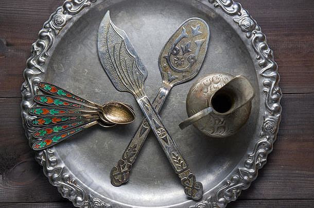 复古的银色厨房用具餐具带有装饰图案的银器，如生动的茶匙、装饰壶，放在深色桌子上的托盘上。顶盎格鲁