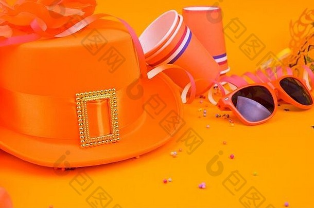 荷兰国王节传统庆典的装饰。明亮背景上的橙色帽子、眼镜、珠宝和五彩纸屑。以画框的形式画。空间。水平格式。