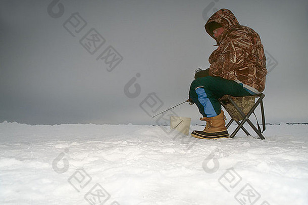 男子坐在雪洞附近冰上钓鱼