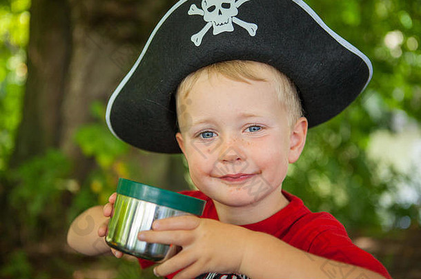 一个4岁的小男孩装扮成海盗，戴着海盗帽，穿着印有恐龙图案的红色T恤。