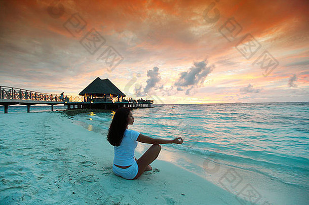 日落时，瑜伽女子在海滩上摆莲花姿势