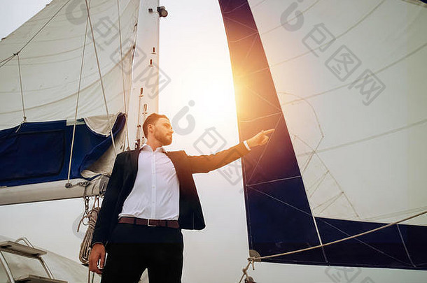 年轻自信的商人用手指着背景中有桅杆的帆船——领导力和远见卓识的商业理念