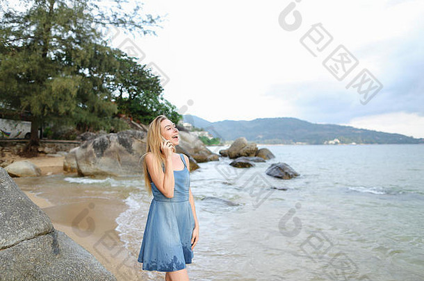 在早晨的海边，一个年轻女孩用智能手机聊天。