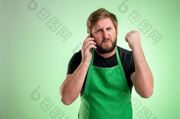 超市员工绿色围裙黑色的t恤不高兴脸手势会说话的手机孤立的绿色背景
