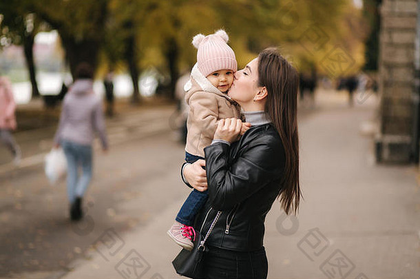 公园里，可爱的小女孩牵着妈手。妈妈和女儿走在外面。金秋幸福家庭