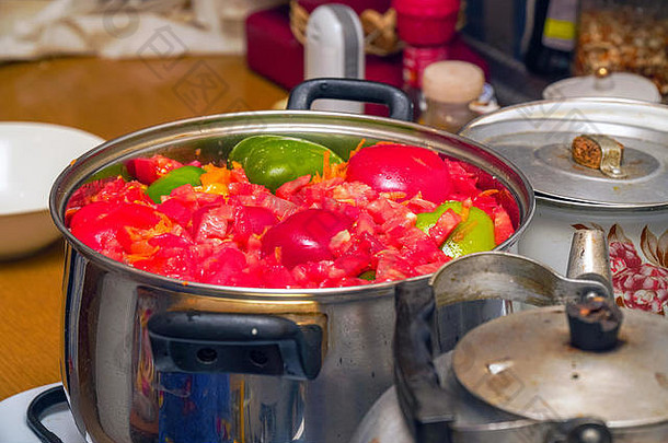 将蔬菜切成小块——甜椒、西红柿等——放在厨房桌子上闪亮的金属锅中