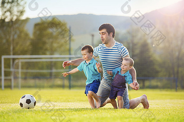 年轻的父亲和他的小儿子在足球场上踢足球