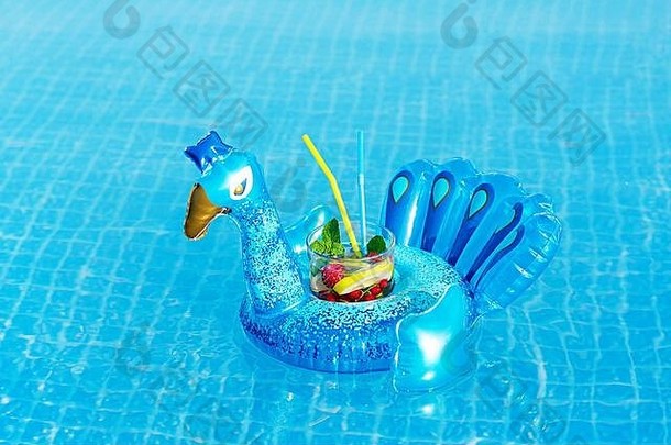 游泳池里充气蓝孔雀玩具上的新鲜椰尾莫吉托。假期的概念。