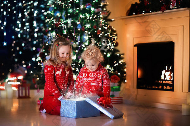 圣诞前夜，一家人在壁炉旁。孩子们打开圣诞礼物。孩子们在圣诞树下拿着礼物盒。