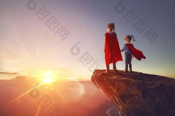 两个小孩正在扮演超级英雄。孩子们在日落的天空中。女孩权力观