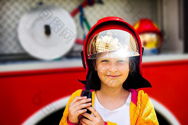 站在消防车前，一个可爱的小女孩正戴着真正的消防员头盔。