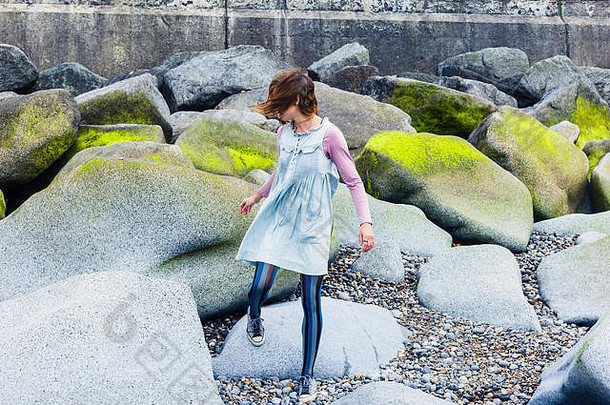 一位年轻女子在海岸上一些生机勃勃的岩石中行走
