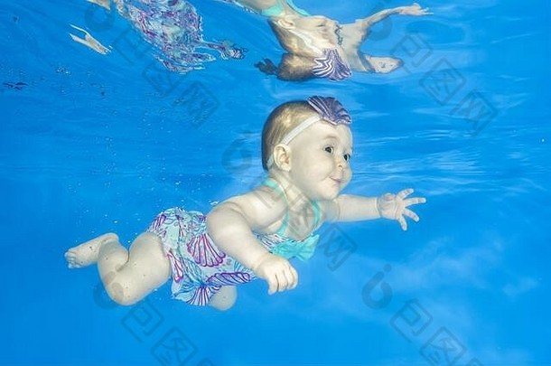 小女孩学会在水下游泳。婴儿在蓝色背景的游泳池里游泳。健康的家庭生活方式和儿童饮水机