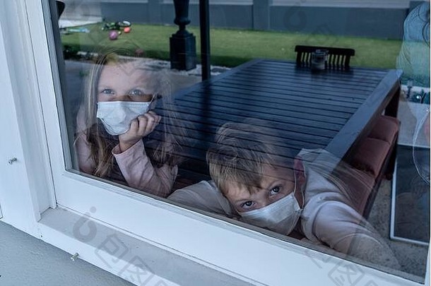 COVID-19停机。在家隔离期间，戴着口罩的悲伤儿童透过窗户看。<strong>学校</strong>关门时，孩子们感到悲伤。科罗纳维鲁