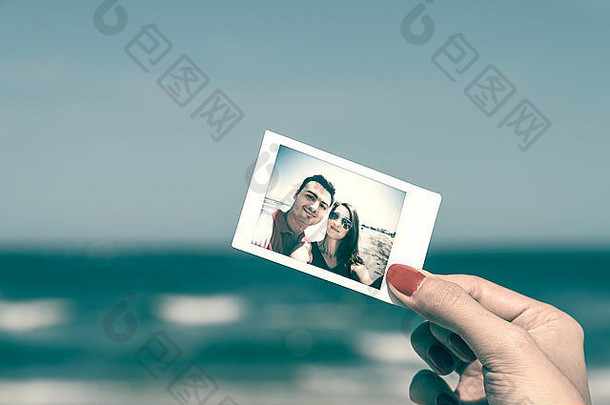 女孩手握着海滩上年轻幸福夫妇的复古即时照片