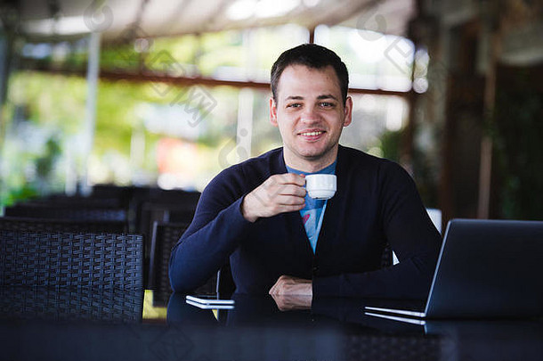 在咖啡馆喝咖啡时，一个英俊的年轻人一边用笔记本电脑一边微笑