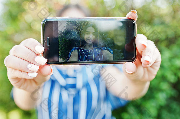 手机在手，漂亮的黑发女孩在屏幕上。