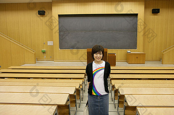 一位年轻女子独自站在教室里对着摄像机微笑