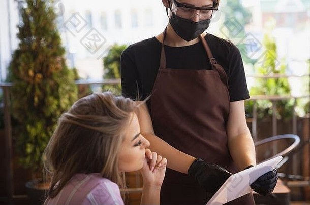 在冠状病毒大流行期间，这位女服务员戴着医用口罩、手套在餐厅工作。代表服务和<strong>安全</strong>的新常态。使用平板电脑进行非接触式点菜。设备、服务。