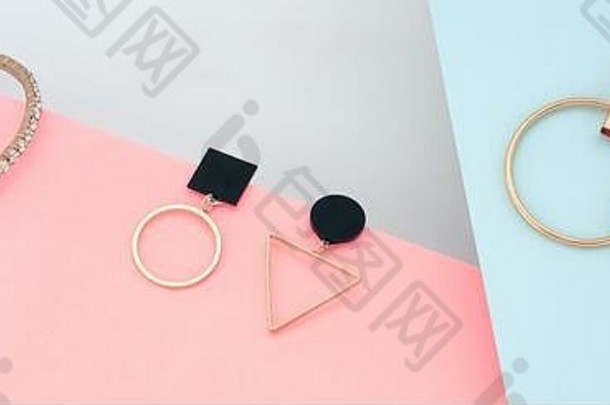 现代黄金首饰几何耳环和手镯平铺在粉色和蓝色的纸上