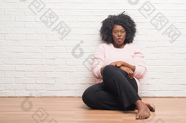 年轻的非洲裔美国妇女坐在家里的地板上，用嘴唇做鱼脸，疯狂而滑稽的手势。滑稽的表情。