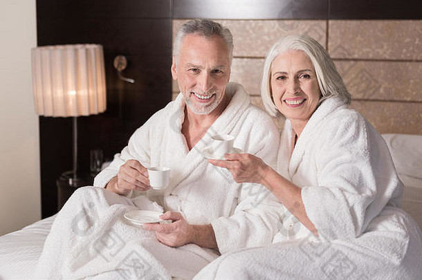 微笑的老夫妇在床上喝咖啡
