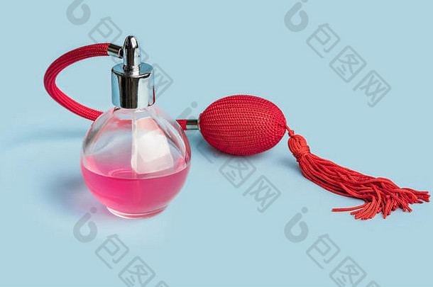 明亮的粉红色香水装在一个透明的玻璃瓶中，红色复古风格的喷雾器，带有气囊和流苏，淡蓝色背景