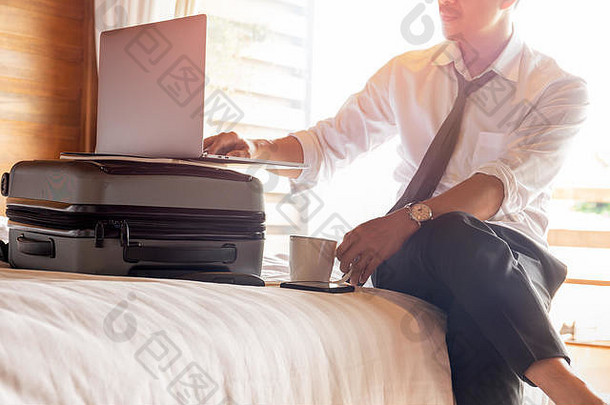 商务旅行时，商人坐在酒店的床上用笔记本电脑工作。