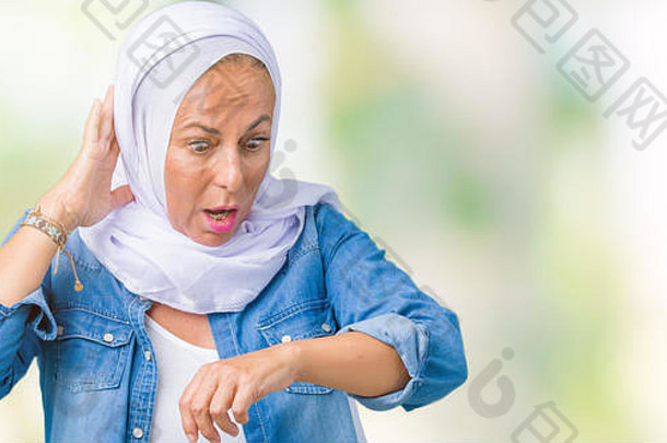 中东阿拉伯中年妇女戴着阿拉伯头巾，隔着孤立的背景看着手表，心急如焚，生怕迟到