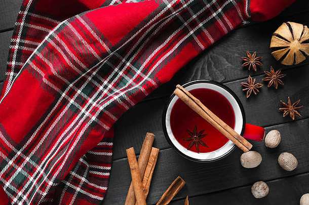 在木制背景上的红色杯子中，放有带香料的圣诞节热葡萄酒。
