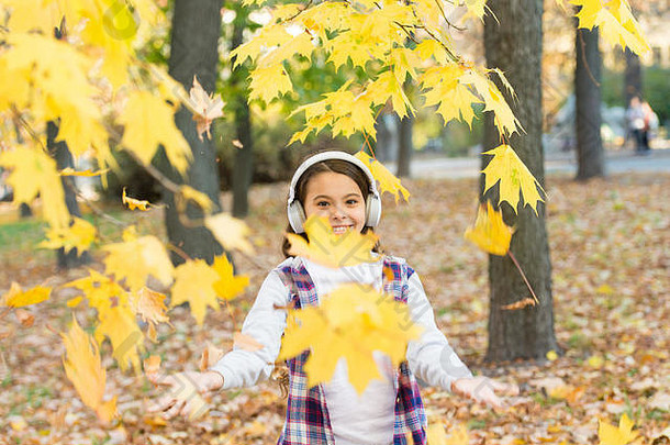 秋天的旋律。听现代耳机的小孩。耳机技术。落叶。快乐的小女孩戴着耳机欣赏秋天的风景。可爱的孩子带着立体声耳机微笑。